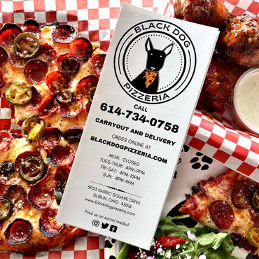 A pizza menu sitting on top of a salad, chicken wings, and a pizza.  