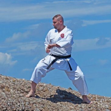 Homme en kimono pratiquant les arts martiaux sur des rochers.