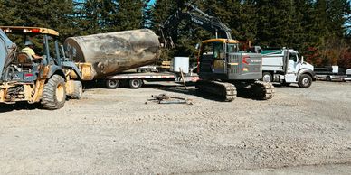 Heavy machinery loading a large log onto a flatbed trailer in a forested area.