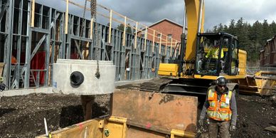 Construction worker and excavator lifting a concrete structure on site.