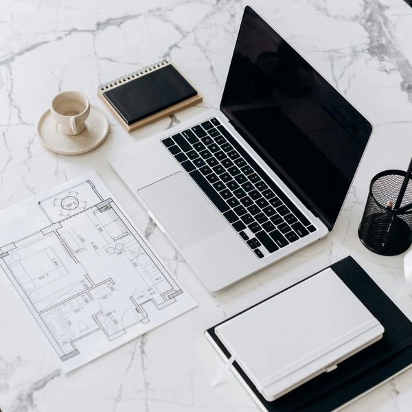 Workspace with laptop, architectural plans, notebooks, and coffee cup on marble table.