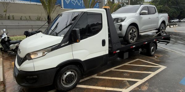 White tow truck carrying a white pickup truck on a rainy day.