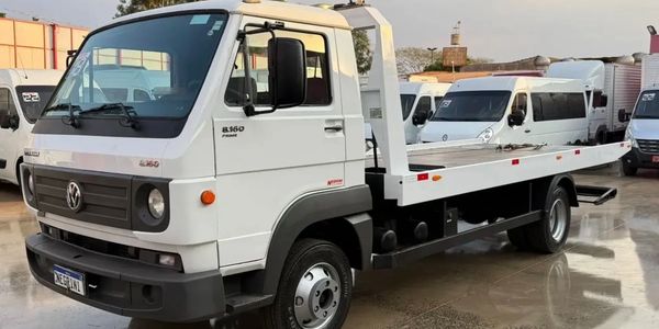 White Volkswagen flatbed tow truck parked outdoors on wet pavement.