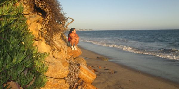 Person sitting on rocks by the beach at sunset.