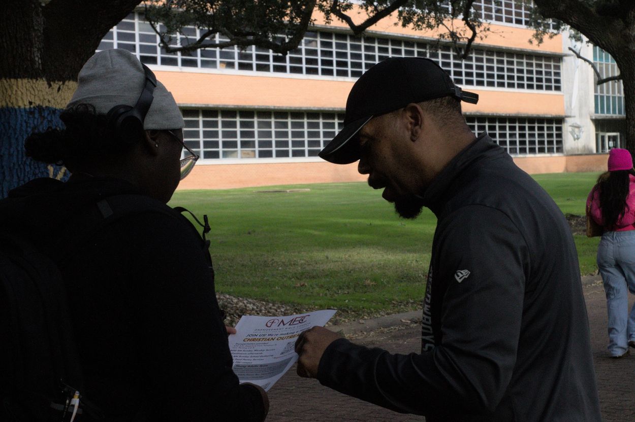 Two people discuss a flyer outdoors near a school building.