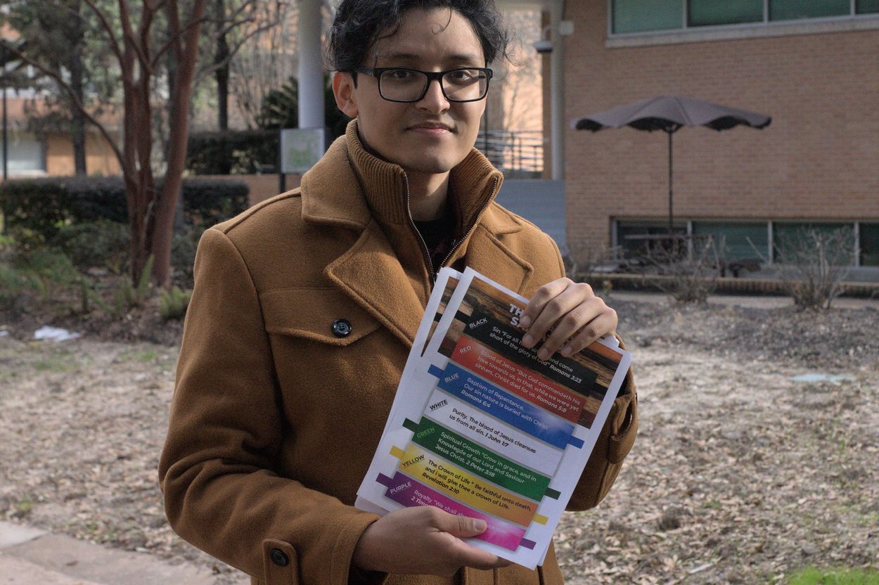 Person in brown coat holding colorful papers outdoors.