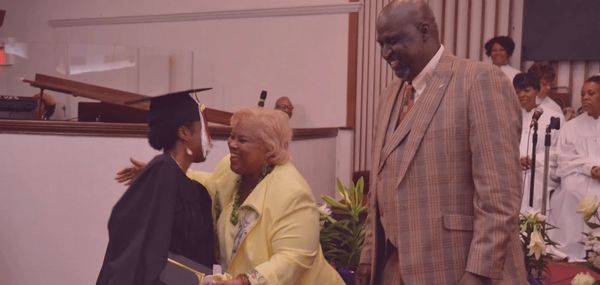 A graduate in cap and gown hugs a woman in a yellow jacket during a ceremony.
