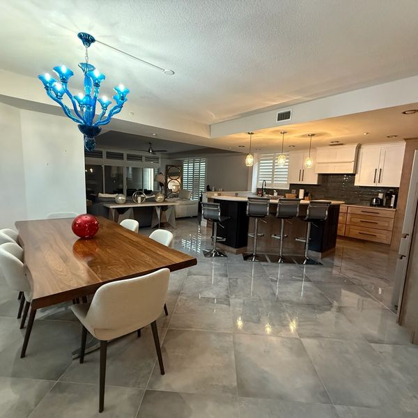 Modern dining and kitchen area with a blue chandelier and wooden table.