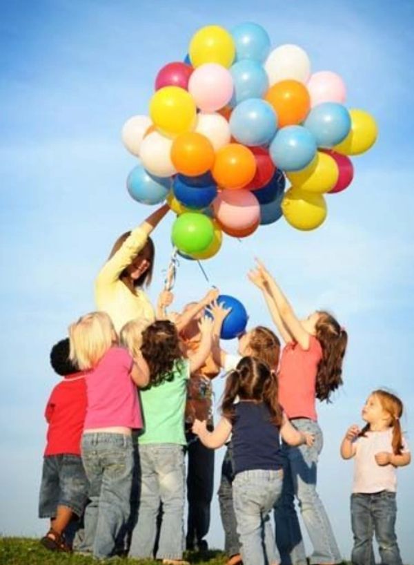 Children joyfully reaching for colorful balloons held by an adult.