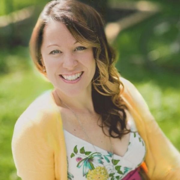 Smiling woman in a floral dress and yellow cardigan outdoors.
