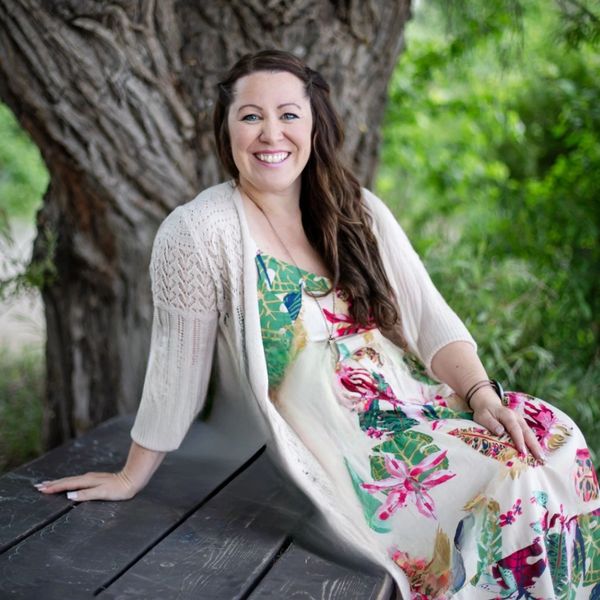 Smiling woman in floral dress sitting on a wooden bench outdoors.