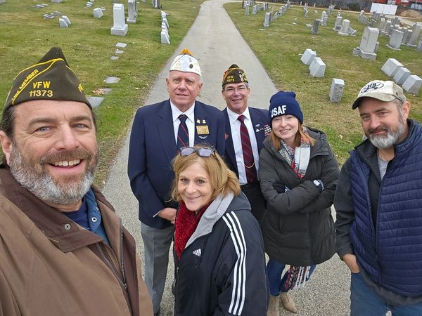A group of veterans and friends smiling in a cemetery.
