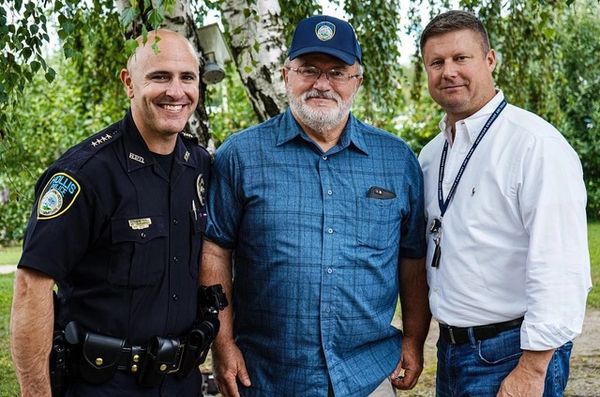 Three men posing outdoors, including a police officer and two casually dressed men.
