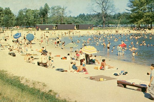 Crowded sandy beach with people swimming and sunbathing on a sunny day.