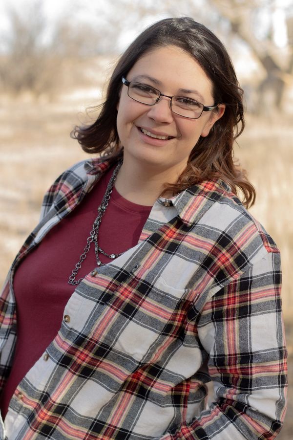 Smiling woman wearing glasses and a plaid shirt outdoors.