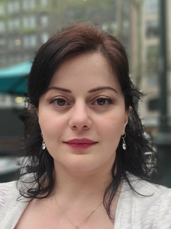 Close-up of a woman with dark hair and earrings outdoors.