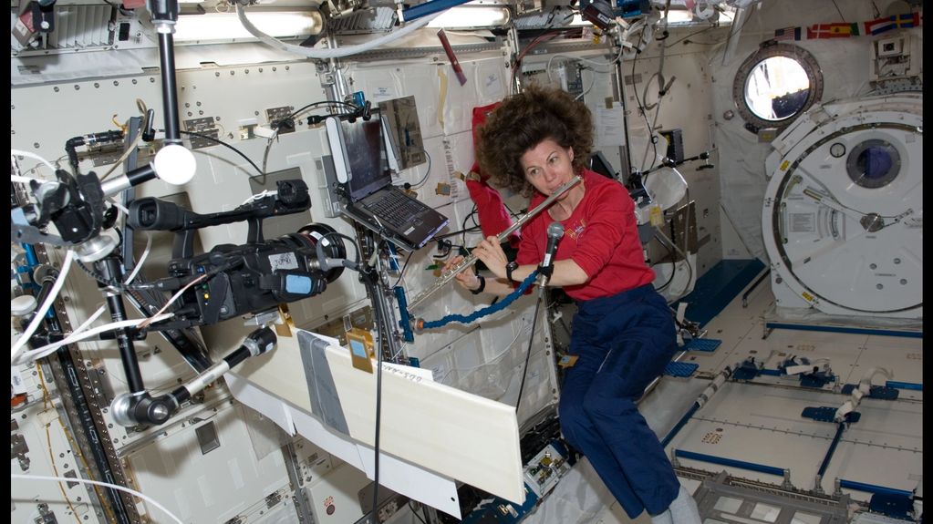 Astronaut playing flute inside the International Space Station with floating hair.
