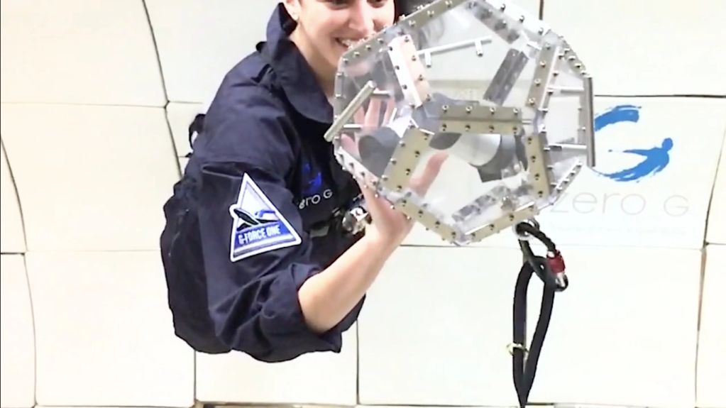 Person in zero gravity holding a geometric object with a harness attached.