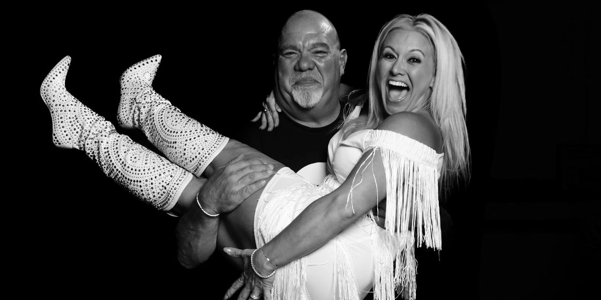 Man happily holding a laughing woman dressed in white with fringed boots.