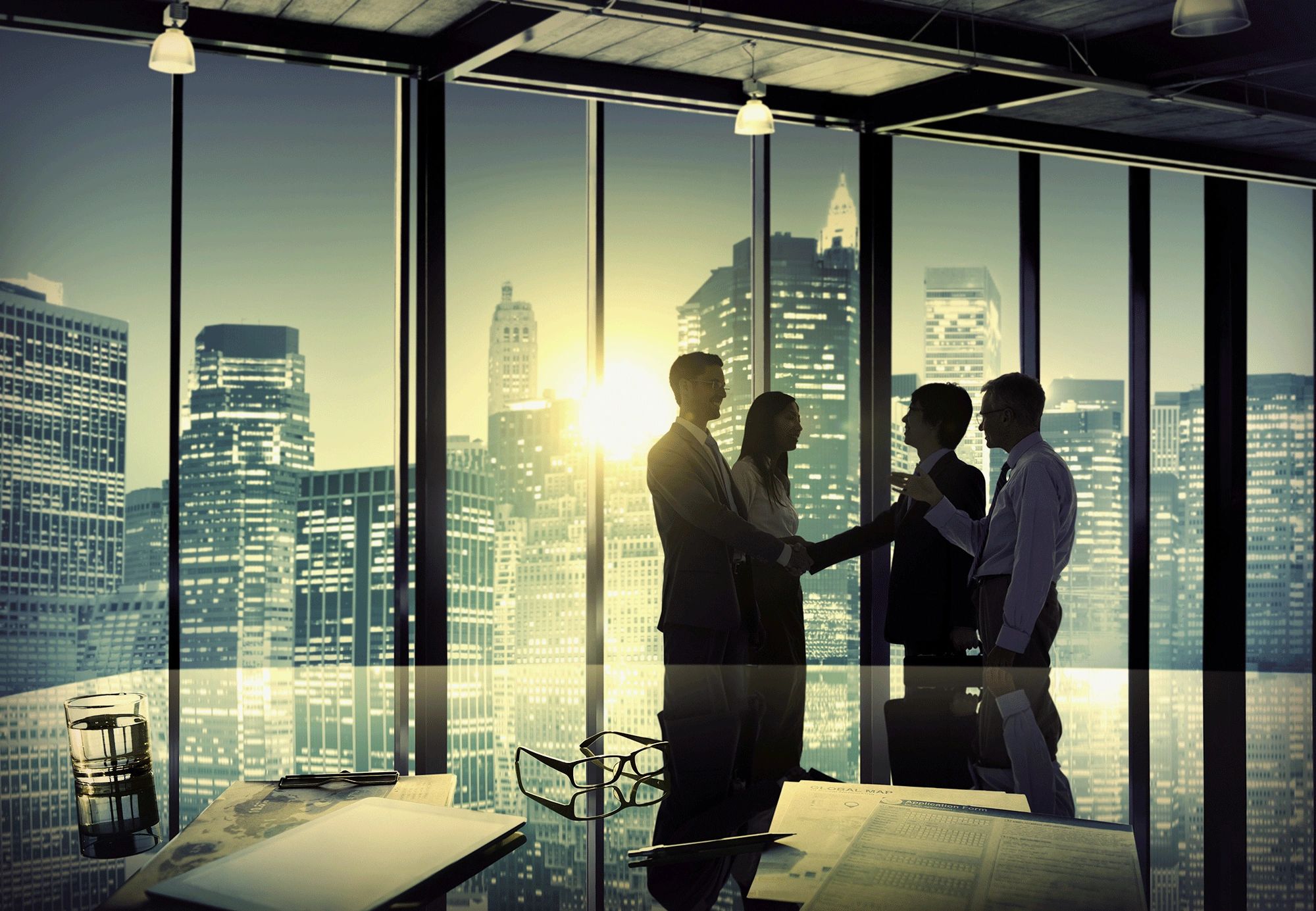 Businesspeople shaking hands in a modern office with city skyline at sunset.