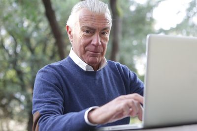 Elderly man using his laptop at an outdoor table, contacting AtHome Helpful RN via website