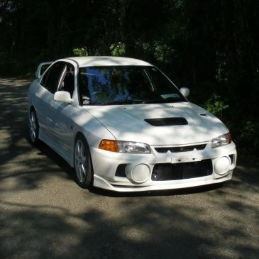 White Mitsubishi Lancer Evolution parked on a shaded road.