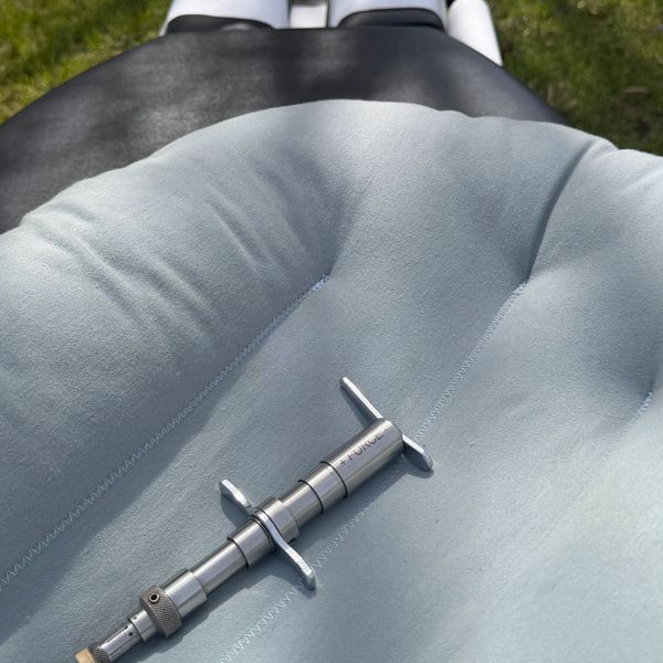 A syringe rests on a padded black medical chair outdoors on grass.
