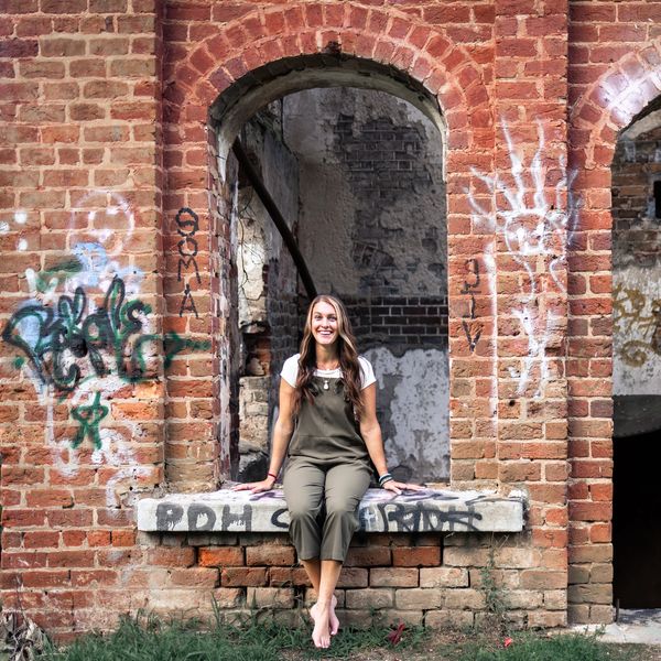 A woman sitting barefoot on a graffiti-covered brick window ledge.