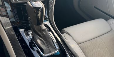 Close-up of a car's automatic gear shift and gray leather seat.