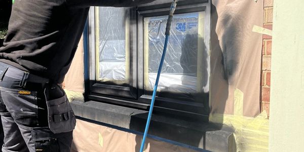Man spray painting a window frame while wearing protective mask and gloves.