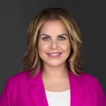 Smiling woman in a bright pink blazer against a dark background.