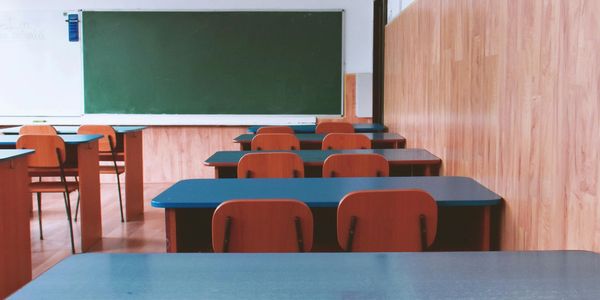 Classroom with 2 chairs pulled up to each table facing a green chalkboard at the front of the room.