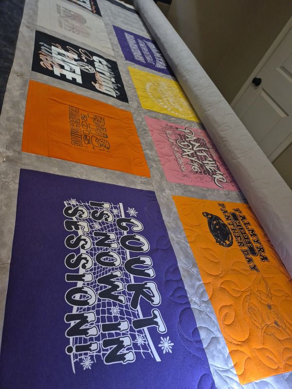 A colorful quilt made from various printed t-shirts with different designs and texts.