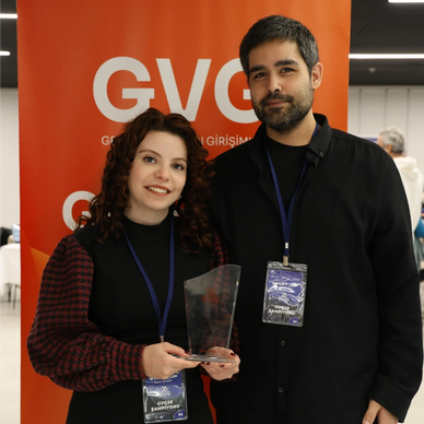 Two individuals holding a trophy, standing in front of an orange GVC banner.