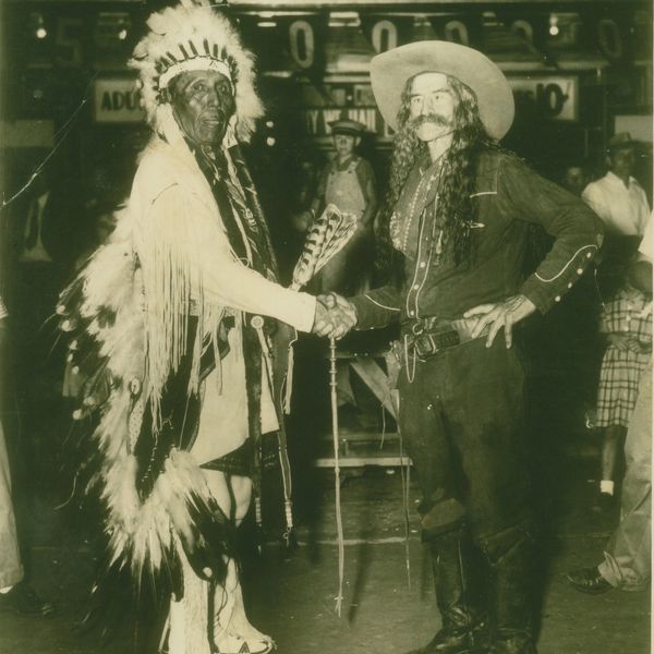 Native American chief and cowboy shaking hands in a historic black-and-white photo.