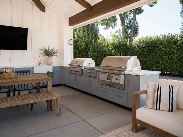 Modern outdoor kitchen with grill, dining table, and seating area under a covered patio.