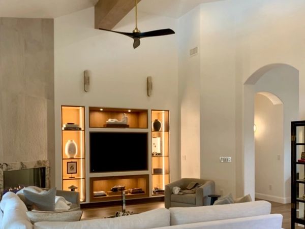 Modern living room with beige sofa and built-in illuminated shelving around TV.