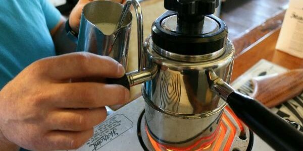 Hand pouring milk into a moka pot on a stovetop.