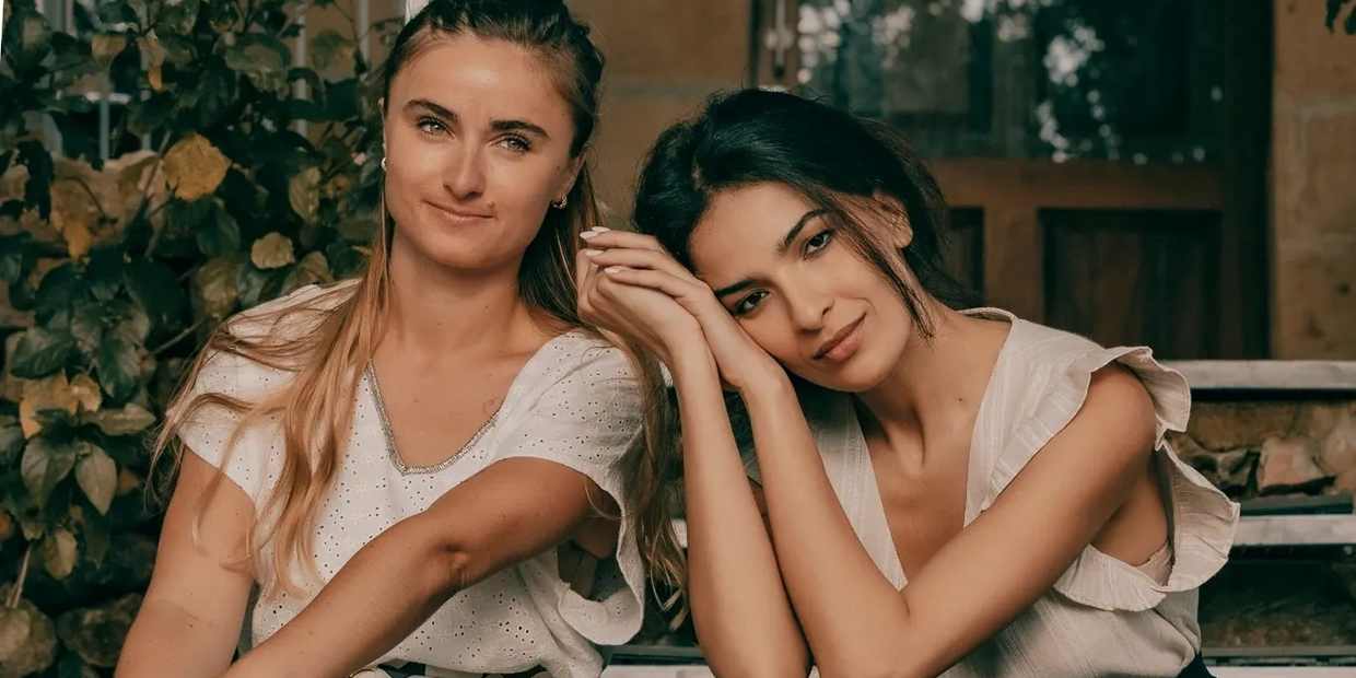 Two women sitting closely together, one resting her head on the other's hand.