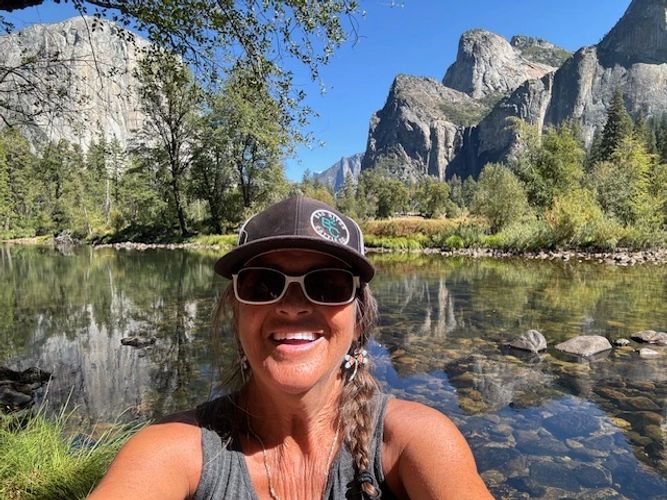 Woman smiling in front of a river and mountains on a sunny day.
