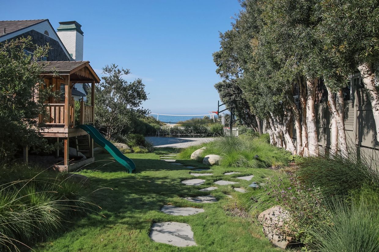 A backyard with a playhouse, slide, and ocean view under clear blue sky.