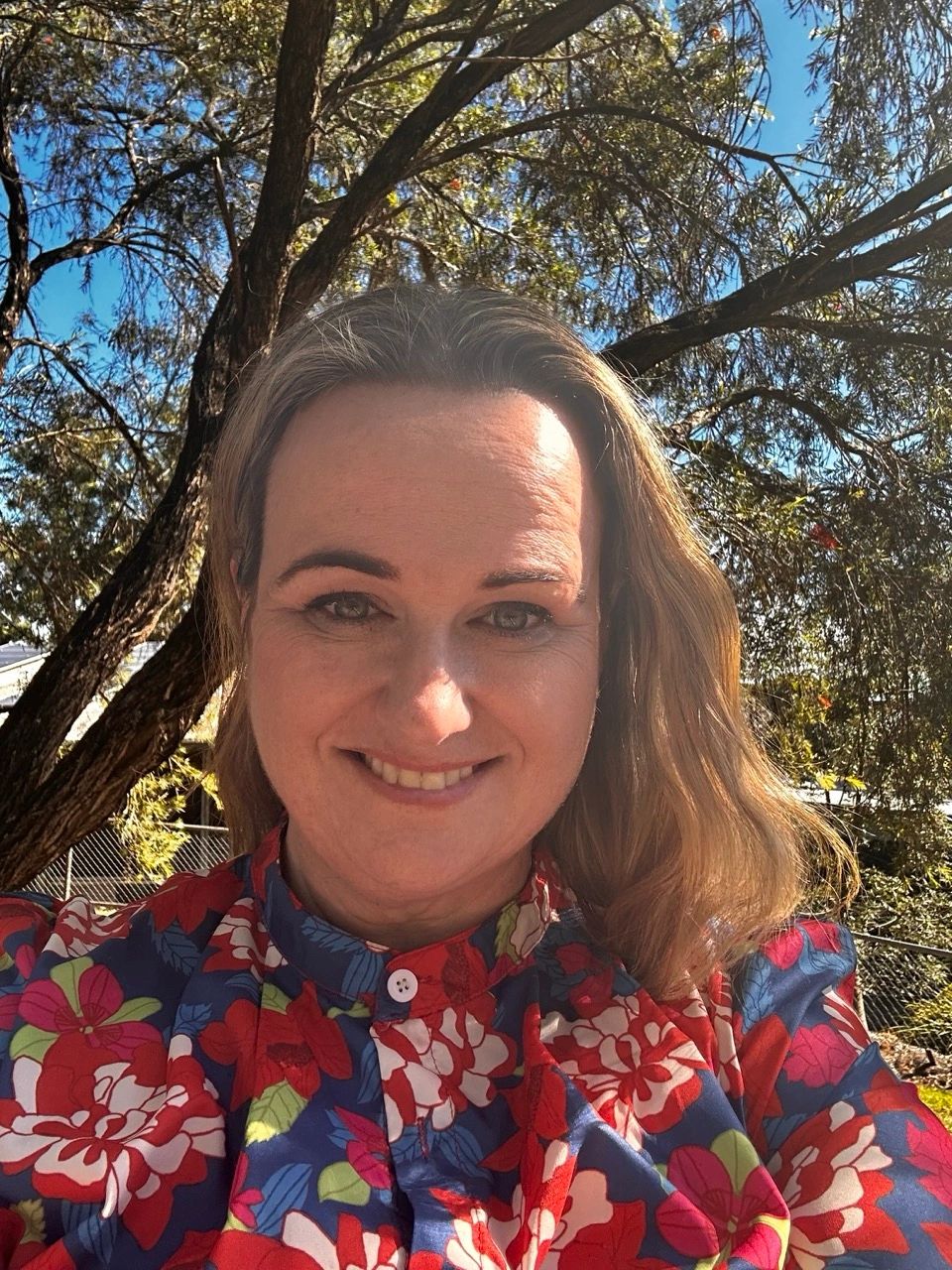 Woman smiling outdoors wearing a floral blouse.