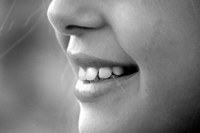 Close-up of a smiling person's mouth and teeth in black and white.