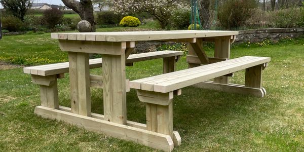 Wooden picnic table set on green grass in a garden.
