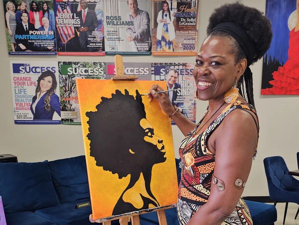 A smiling woman painting a silhouette portrait on a canvas indoors.