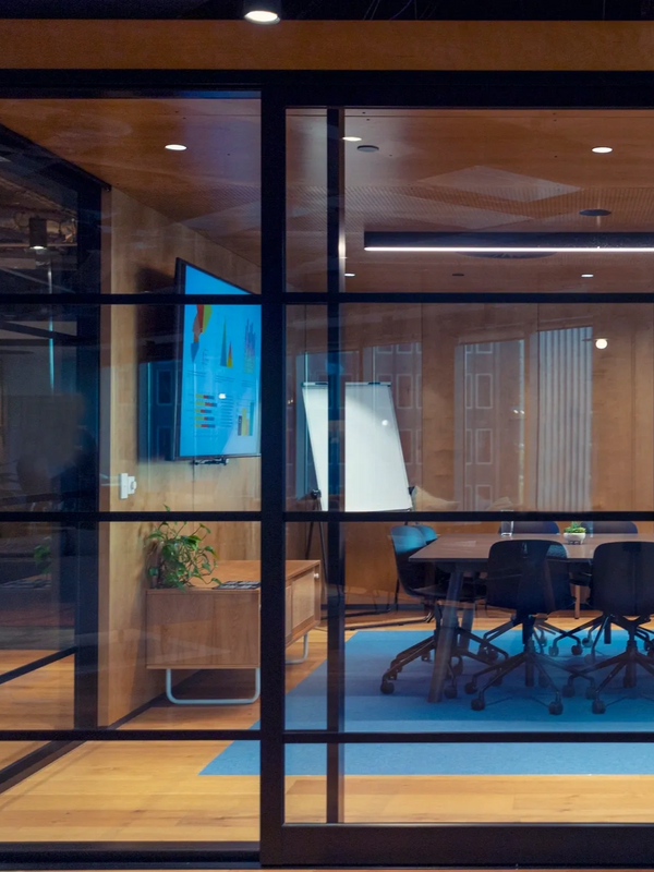 Man working alone in modern glass-walled conference room with charts on screen.