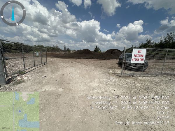 Empty dirt lot behind a chain-link fence with a sign.