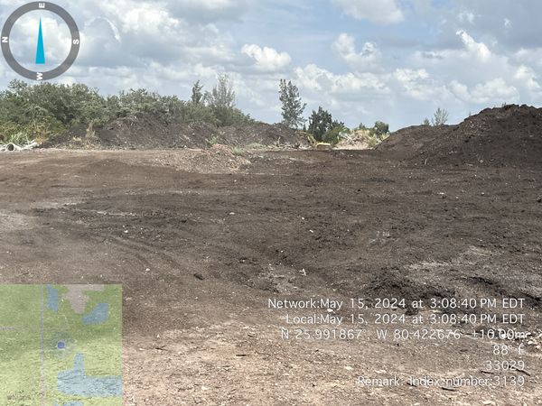 Cleared land with some plants and a partly cloudy sky.