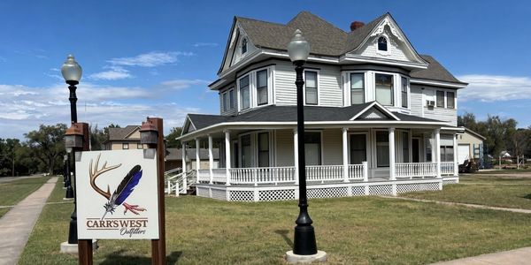 Large Victorian house with a CarrsWest Outfitters sign.