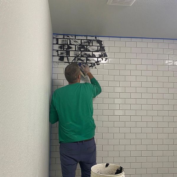 A man applying black grout to white subway tiles in a bathroom.